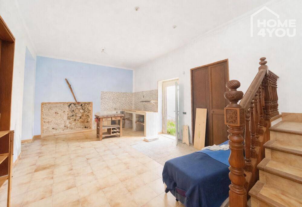 Unfertige Küche mit Fliesenboden, freigelegter Steinwand und Holztreppe, bereit zur Renovierung.