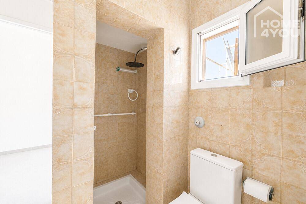 Badezimmer mit beigen Fliesen, Duschbereich und Fenster für natürliches Licht.