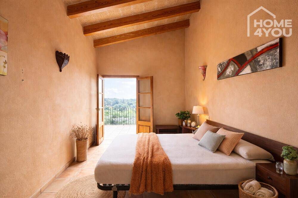 Helles Schlafzimmer mit Holzbalkendecke, Fliesenboden und Zugang zum Balkon mit Weitblick.