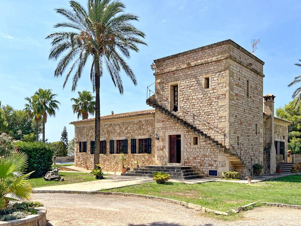Traditionelles Steinhaus mit markantem Turm und Außentreppe, umgeben von mediterraner Vegetation.