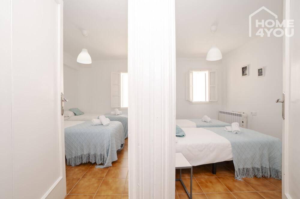 Blick in zwei helle Schlafzimmer mit jeweils zwei Einzelbetten und Fliesenboden.