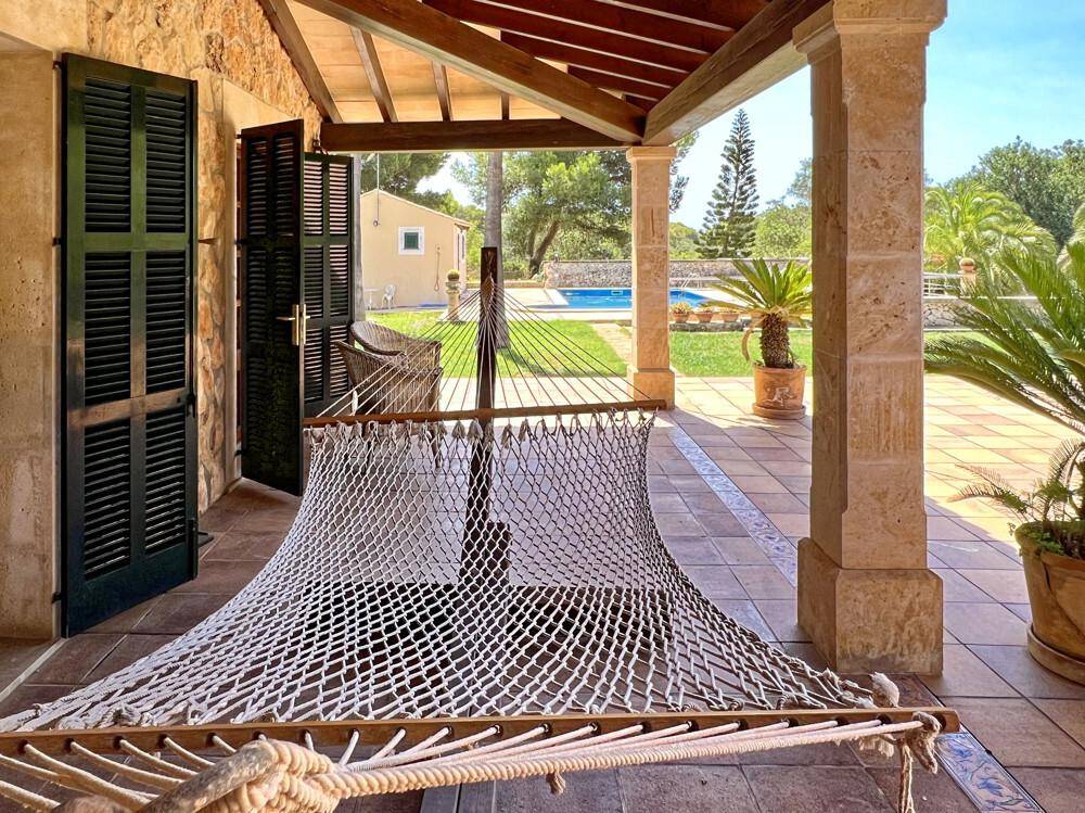 Gemütliche überdachte Terrasse mit Hängematte, Blick auf den Garten und den Poolbereich.