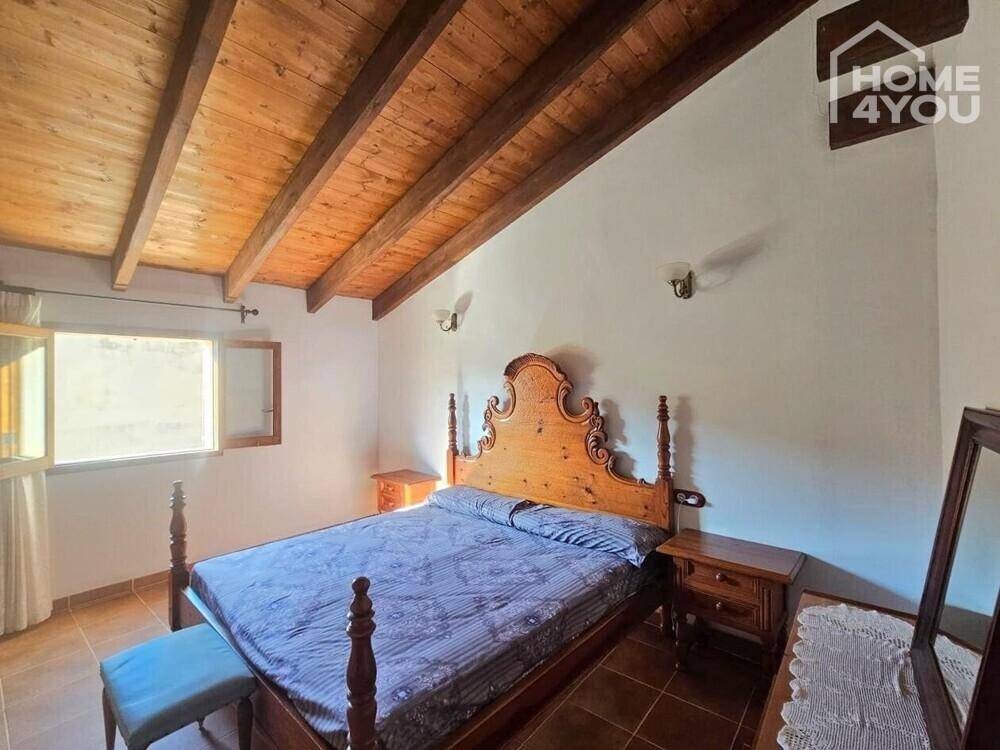 Schlafzimmer mit großem Holzbett, Fliesenboden und rustikaler Holzbalkendecke.