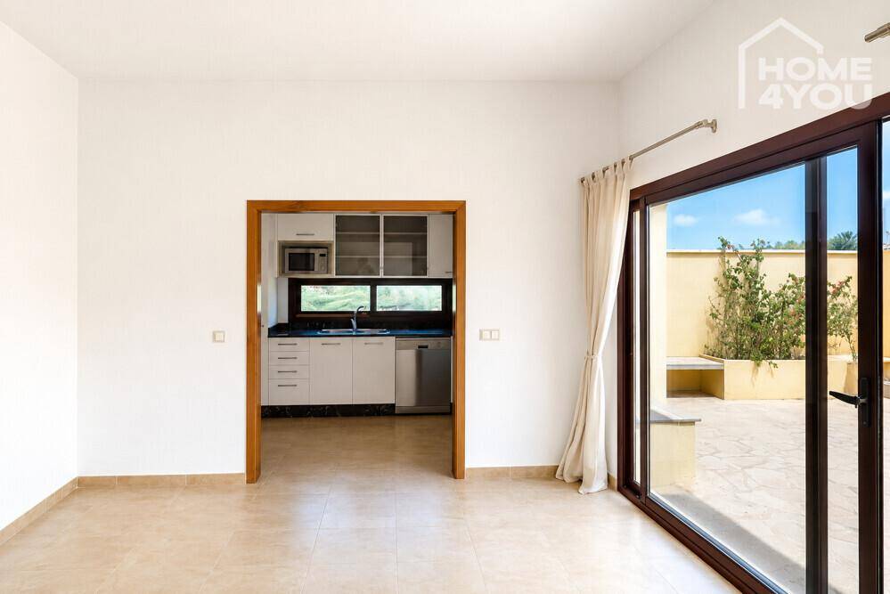 Wohnbereich mit Blick auf eine separate Küche und Zugang zu einer sonnigen Außenterrasse.