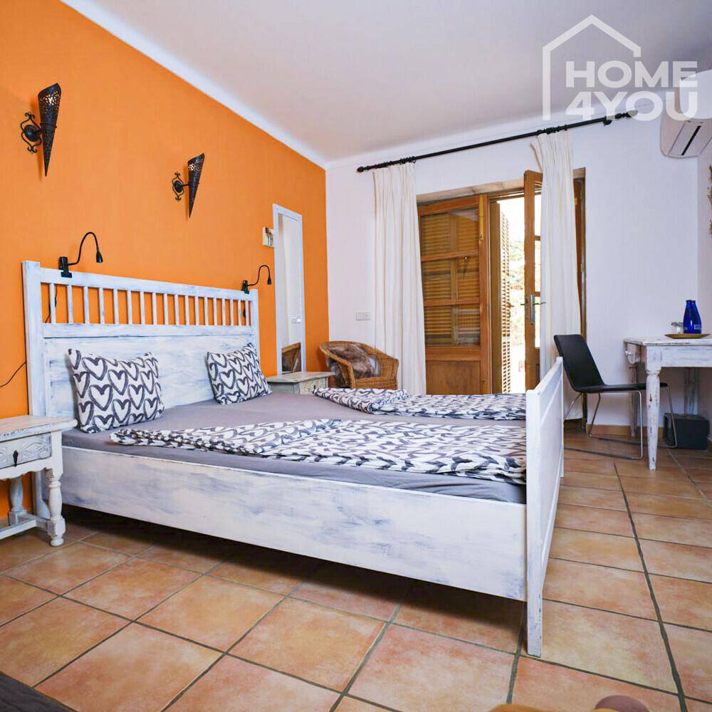 Schlafzimmer mit orangefarbener Wand, weißem Bett und Zugang zum Außenbereich.