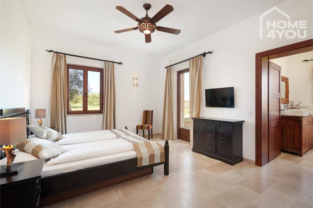 Geräumiges Schlafzimmer mit Deckenventilator, Fliesenboden und Blick ins Grüne.