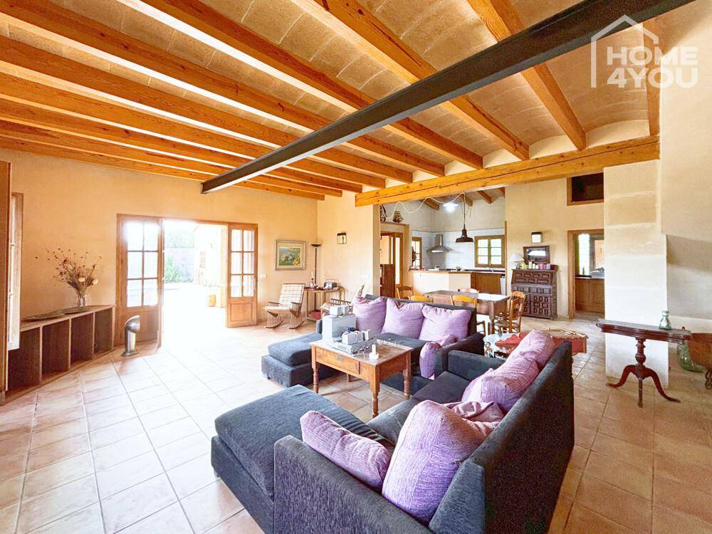 Geräumiges Wohn-Esszimmer mit sichtbaren Holzbalken, bequemen Sofas und Blick ins Grüne.