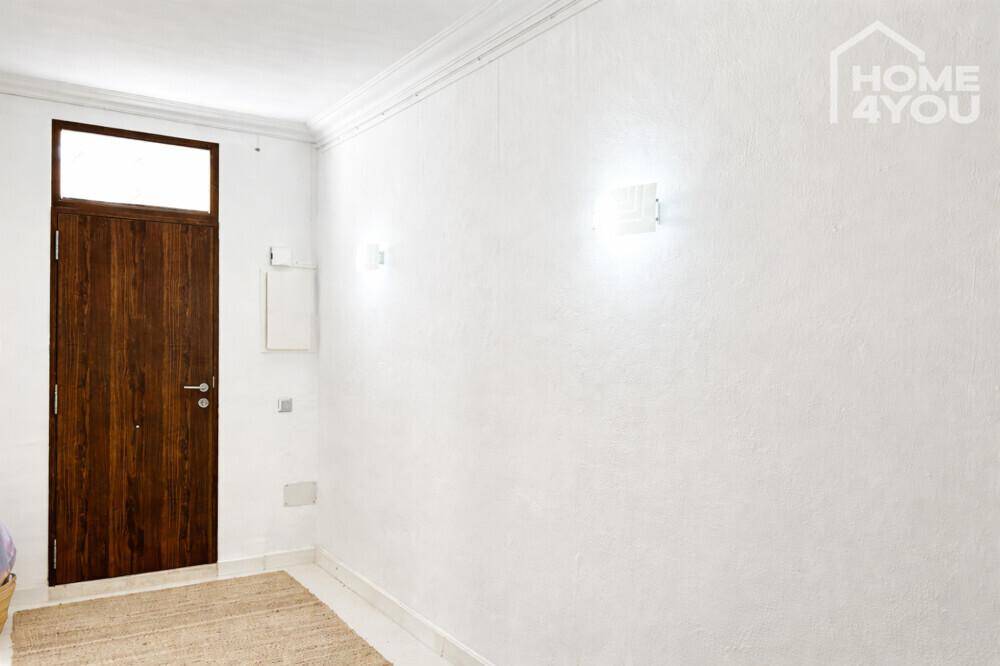 Heller Flur mit Holztür und Wandleuchten, der zu weiteren Räumen führt.