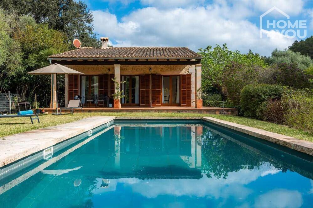 Charmantes Haus mit großem Pool und weitläufigem Gartenbereich unter strahlend blauem Himmel.