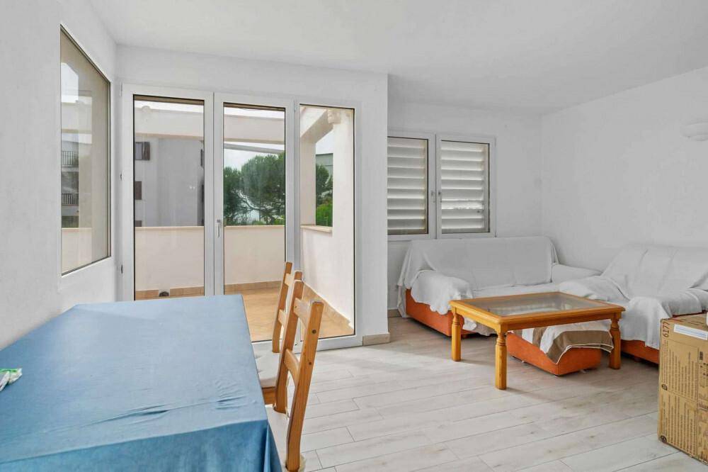 Heller Wohn- und Essbereich mit hellem Holzboden und Zugang zu einem kleinen Balkon.