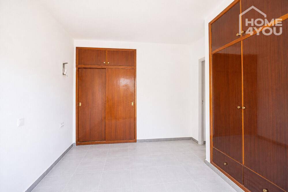 Schlafzimmer mit zwei großen Holzschränken, Fliesenboden und weißen Wänden.