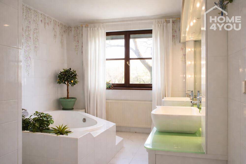 Helles Badezimmer mit Eckbadewanne, Doppelwaschbecken und Fenster.