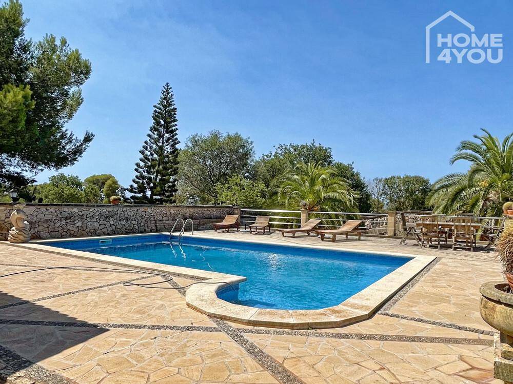 Großzügiger Poolbereich mit Liegestühlen und Essgelegenheit, umgeben von Natursteinpflaster und mediterraner Vegetation.