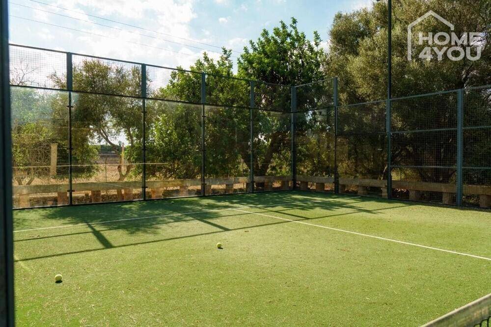 Padel-Tennisplatz mit Kunstrasen und hohen Zäunen, umgeben von Bäumen.