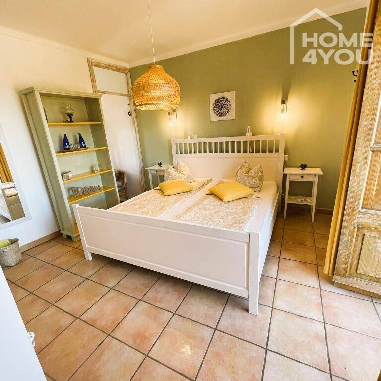 Helles Schlafzimmer mit grün gestrichener Wand, Holzbett und gefliestem Boden.