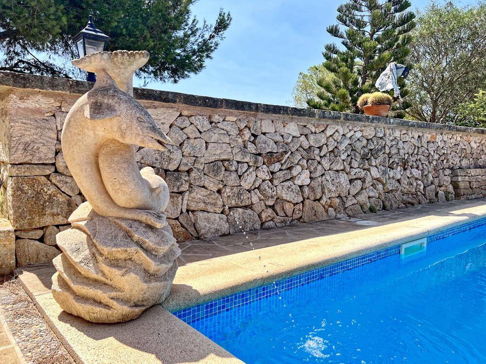 Dekorative Steinskulptur am Rande des Pools mit blauen Mosaikfliesen und einer Steinmauer im Hintergrund.