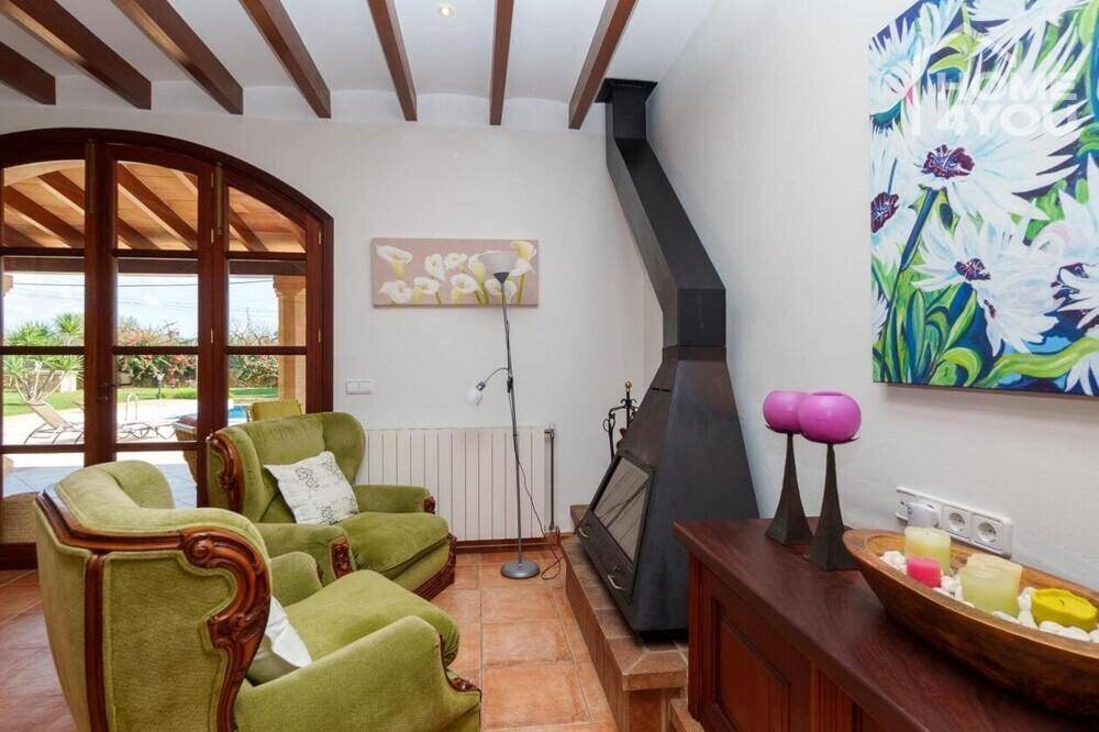 Gemütliches Wohnzimmer mit Kamin, grünen Sesseln, Holzbalkendecke und Poolblick.