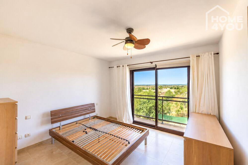 Helles Schlafzimmer mit Deckenventilator, Fliesenboden und Zugang zu einem Balkon mit grüner Aussicht.