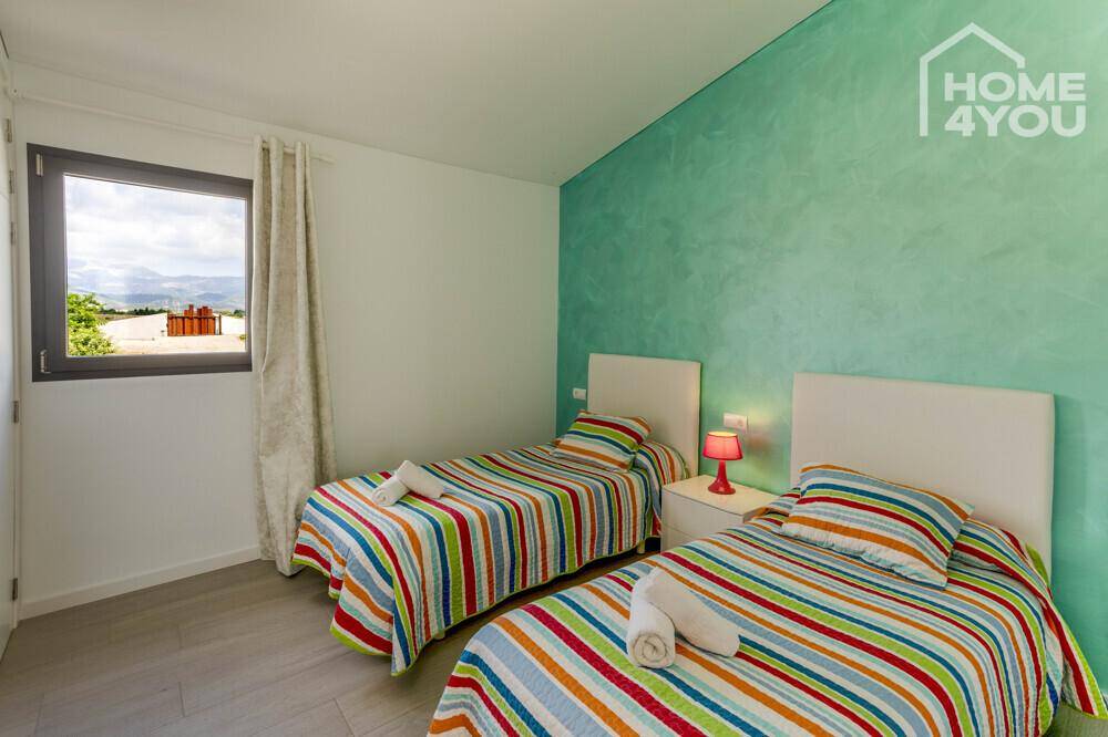 Helles Schlafzimmer mit zwei Einzelbetten, farbenfroher Bettwäsche und grüner Akzentwand.