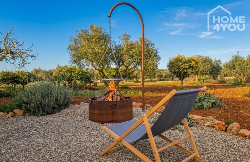 Gemütlicher Gartenbereich mit Feuerstelle und Liegestuhl unter blauem Himmel.