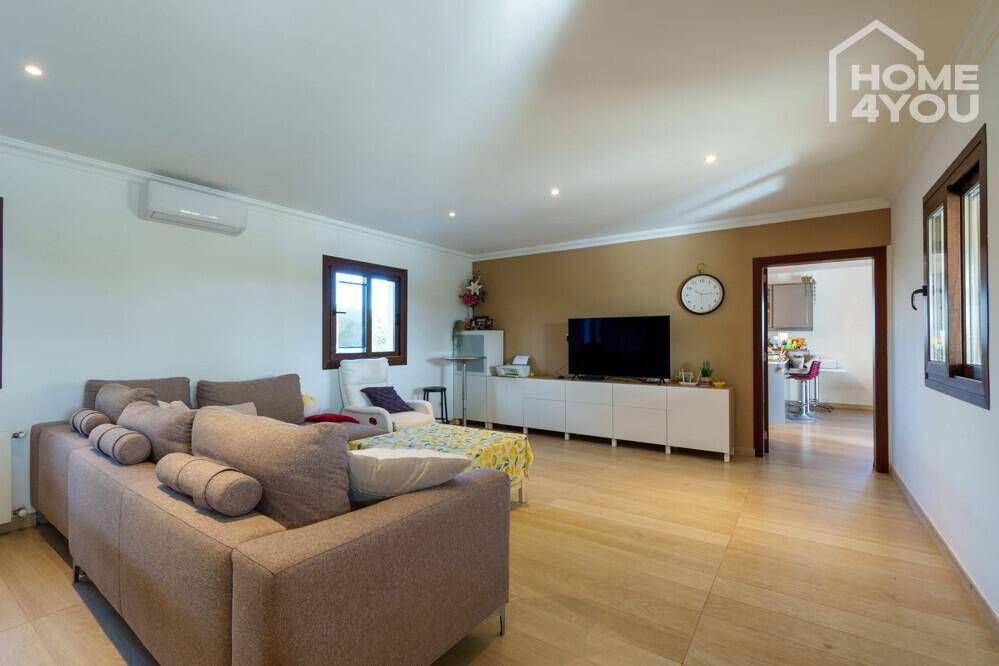 Helles Wohnzimmer mit beigem Sofa, Fliesenboden und Klimaanlage, offen zu einem weiteren Raum.