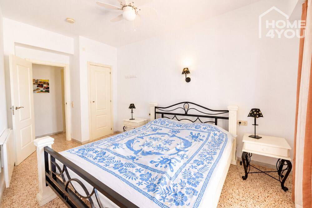 Helles Schlafzimmer mit Doppelbett, Nachttischen und Zugang zu einem weiteren Raum.