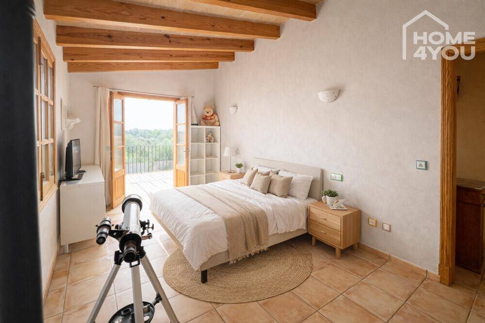 Gemütliches Schlafzimmer mit Holzbalkendecke, Fliesenboden und direktem Zugang zum Balkon.