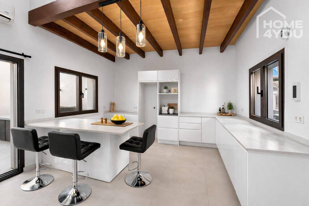 Moderne, helle Küche mit weißer Einrichtung, Kücheninsel und rustikalen Holzbalken an der Decke.
