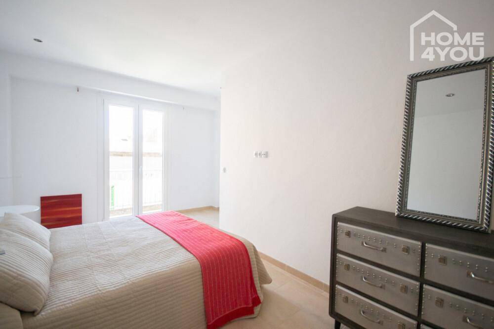 Helles Schlafzimmer mit Doppelbett, Kommode und Zugang zu einem französischen Balkon.