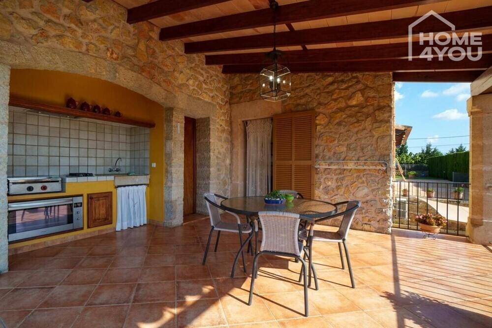 Geräumige überdachte Terrasse mit Außenküche, Essbereich und traditionellen Steinwänden.