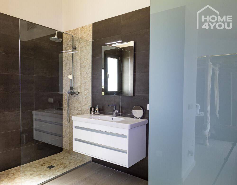 Elegantes Badezimmer mit begehbarer Dusche, modernem Waschtisch und dunklen Fliesen.