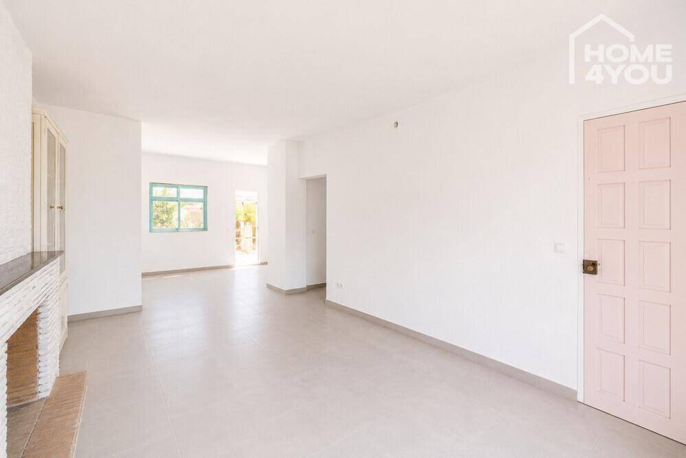Helles Wohnzimmer mit hellen Fliesen, weißen Wänden und einem rosafarbenen Türblatt.
