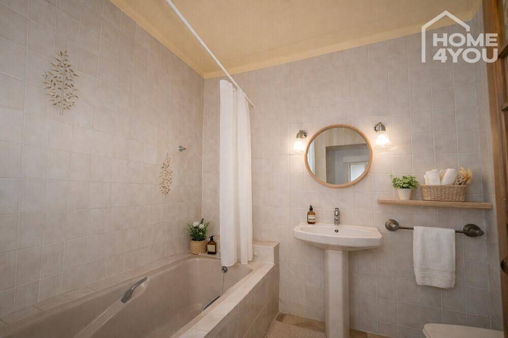 Gefliestes Badezimmer mit Badewanne, Standwaschbecken und rundem Spiegel.