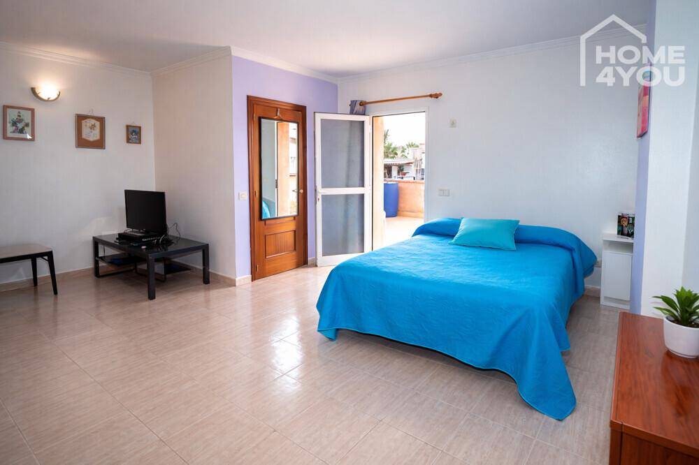 Helles Schlafzimmer mit blauem Bett und Fernseher, mit direktem Zugang zu einer Terrasse.