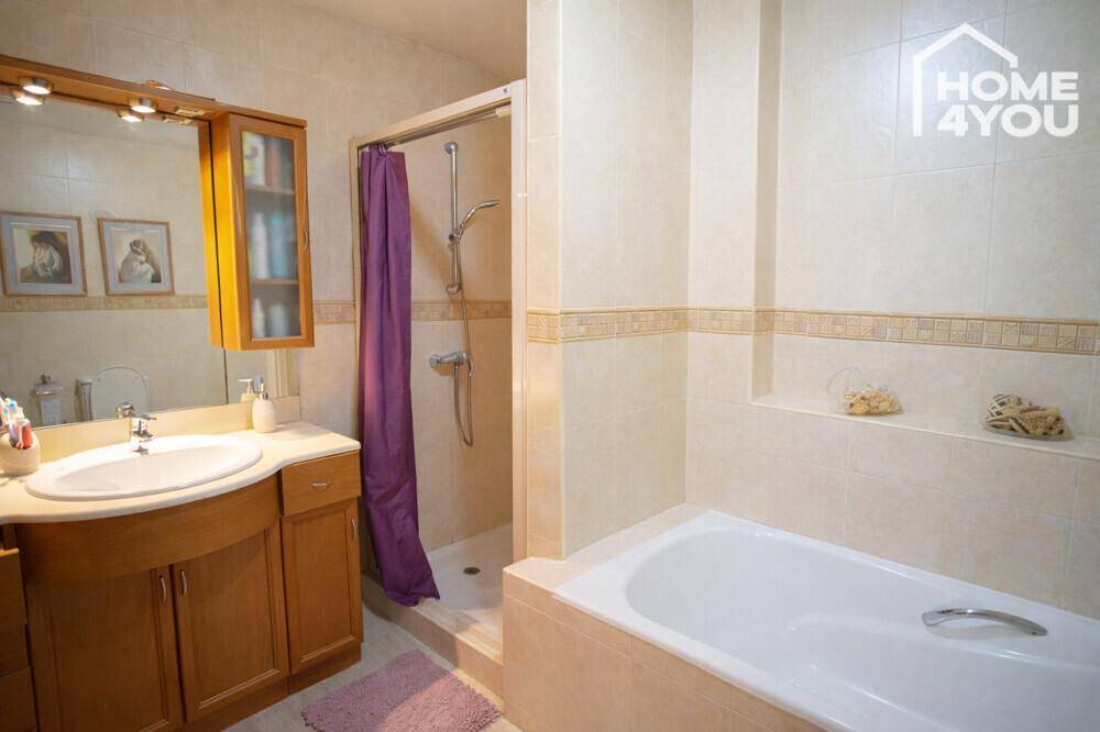 Badezimmer mit Waschtisch, Dusche und Badewanne, ausgestattet mit beigefarbenen Fliesen.