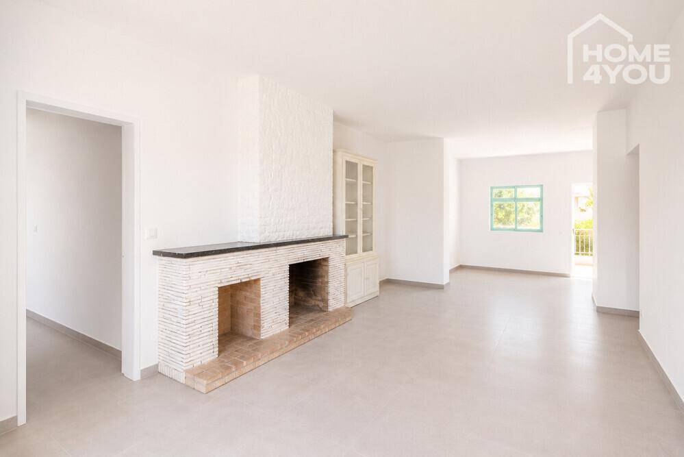 Geräumiges Wohnzimmer mit Kamin, weißen Wänden und hellen Fliesenboden.