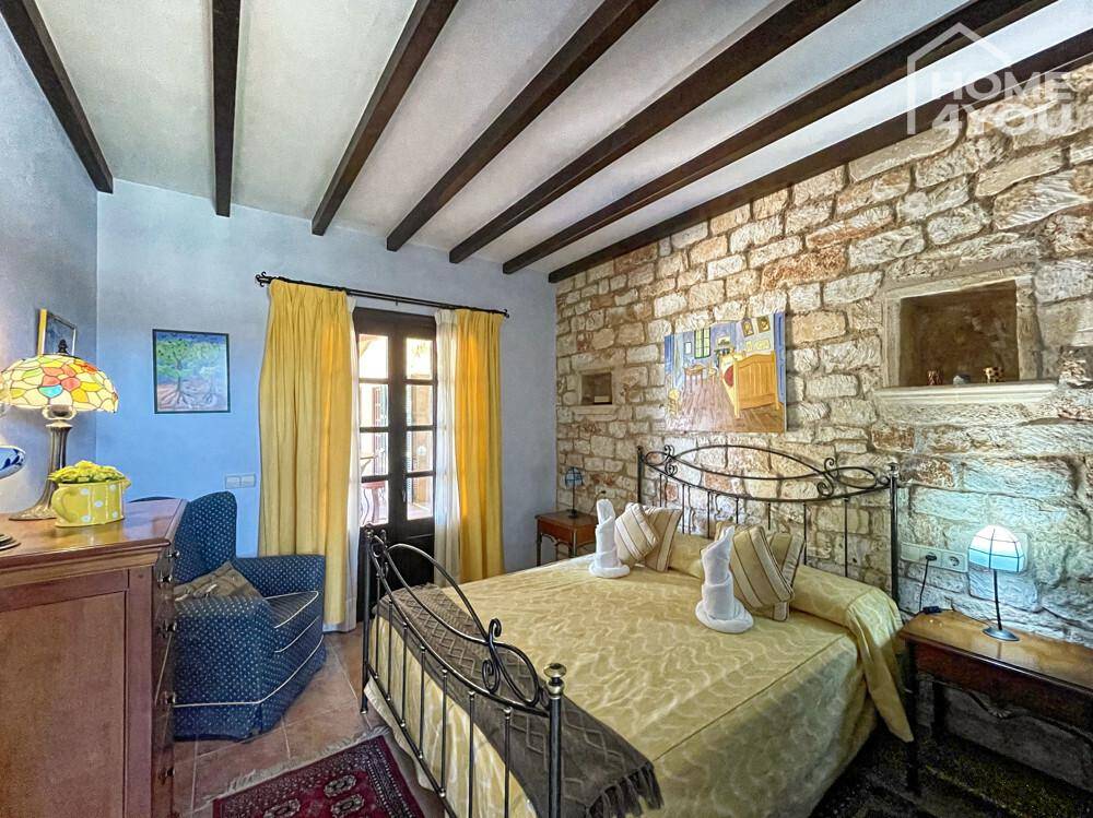 Rustikales Schlafzimmer mit freiliegenden Holzbalken, Steinwand und schmiedeeisernem Bettgestell.