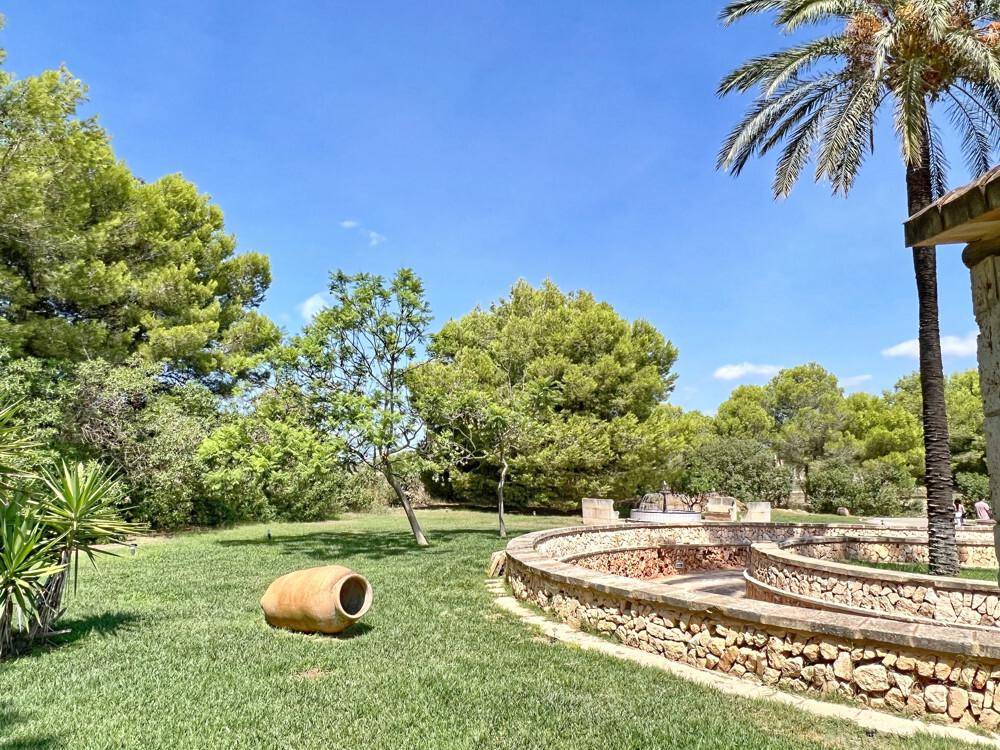 Gepflegter Gartenbereich mit Rasen, geschwungener Steinmauer und einem großen Terrakotta-Gefäß.
