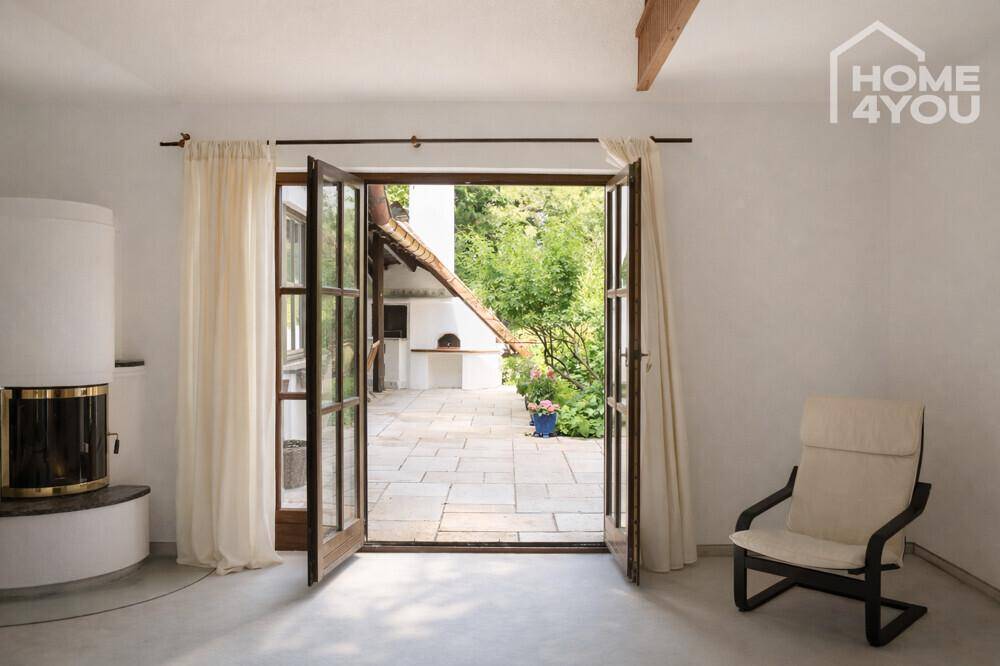 Heller Raum mit Kaminofen und geöffneten Türen, die auf eine gepflasterte Terrasse führen.