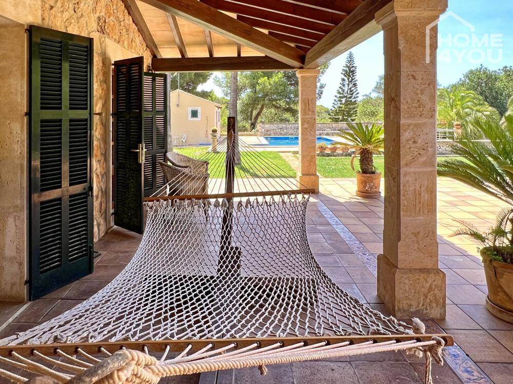 Gemütliche überdachte Terrasse mit Hängematte, Blick auf den Garten und den Poolbereich.