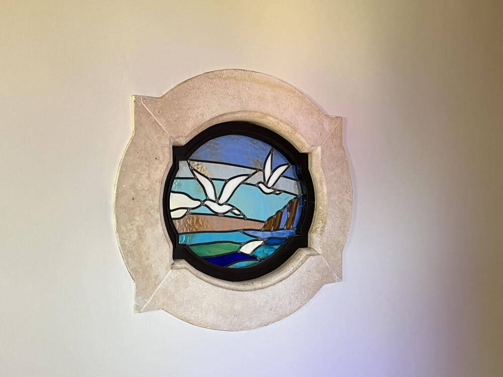 Rundes Buntglasfenster mit maritimen Motiven, das natürliches Licht in den Raum bringt.