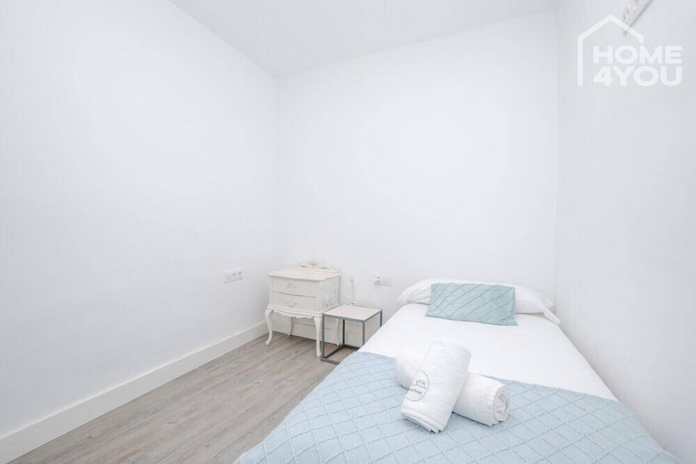 Helles, minimalistisches Schlafzimmer mit Einzelbett, weißen Wänden und modernem Laminatboden.