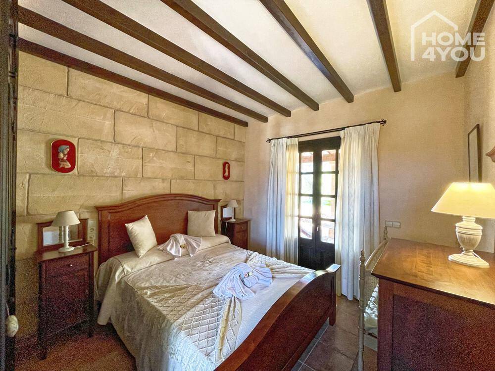 Traditionelles Schlafzimmer mit Steinwand, Holzbalken und einem großen Doppelbett.