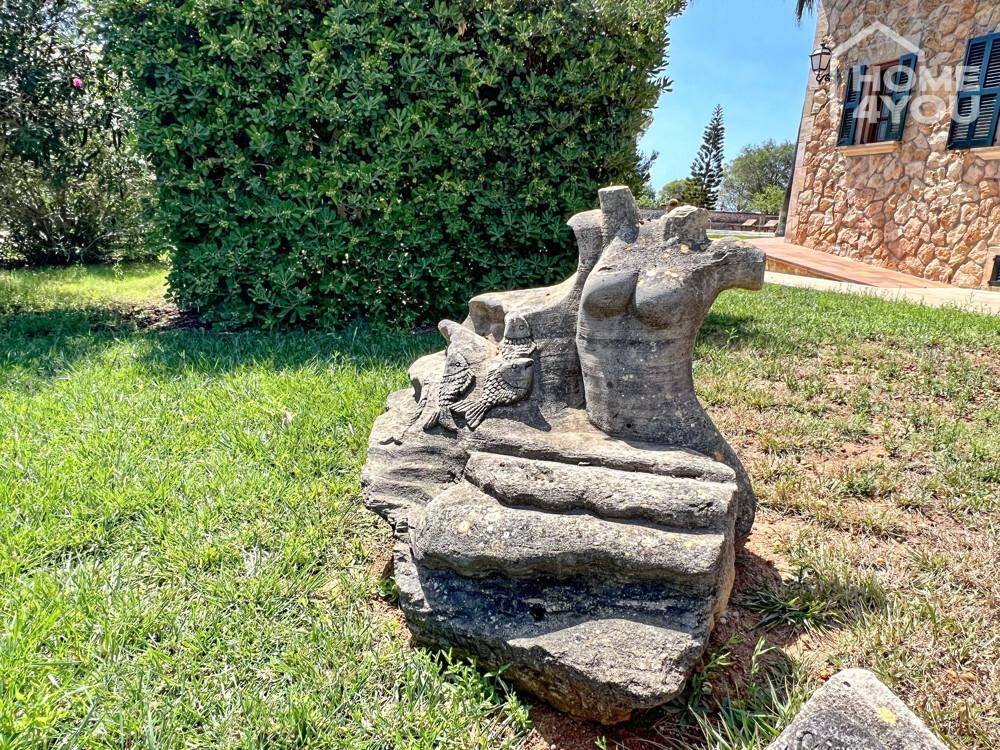 Detailaufnahme einer steinernen Skulptur im grünen Gartenbereich des Anwesens.