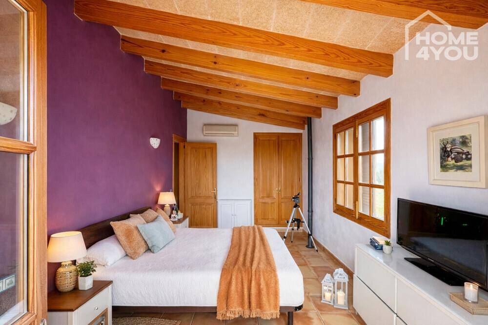 Helles Schlafzimmer mit Holzbalkendecke, farbiger Akzentwand und Zugang zum Balkon.