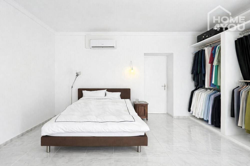 Helles Schlafzimmer mit Bett, Klimaanlage und offenem Kleiderschrank mit Kleiderstangen.