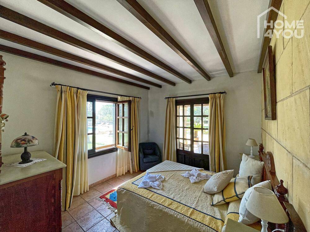 Helles Schlafzimmer mit Holzbalkendecke, Fliesenboden und Blick auf den grünen Garten.
