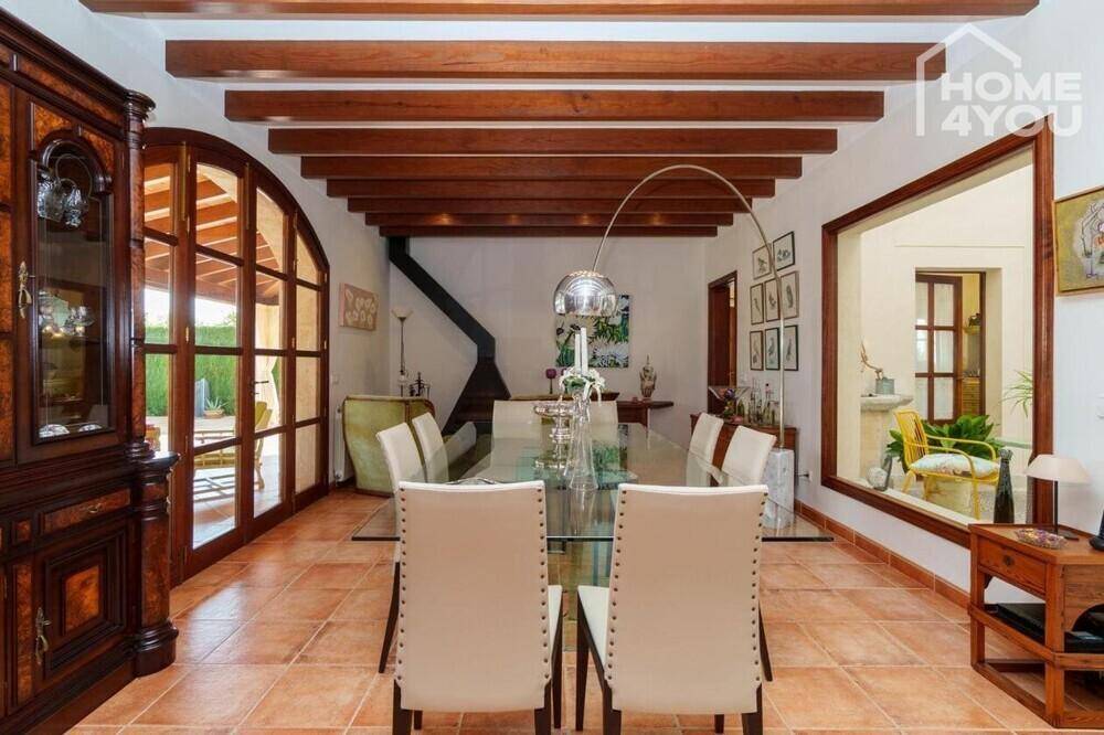 Eleganter Essbereich mit großem Glastisch, Holzbalkendecke und Zugang zur überdachten Terrasse.