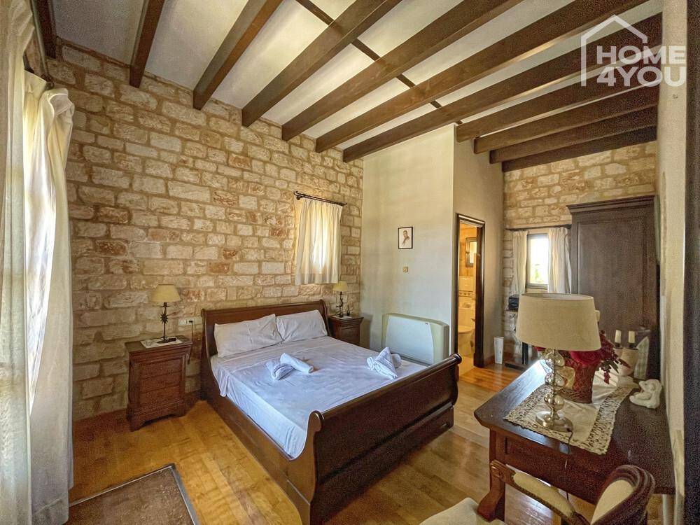 Gemütliches Schlafzimmer mit freiliegenden Holzbalken, Steinwand und traditionellem Holzdoppelbett.