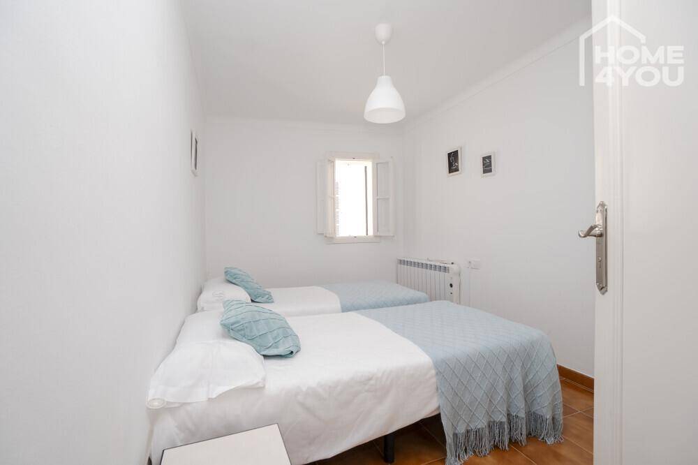Helles Schlafzimmer mit zwei Einzelbetten, Fenster und traditionellem Fliesenboden.